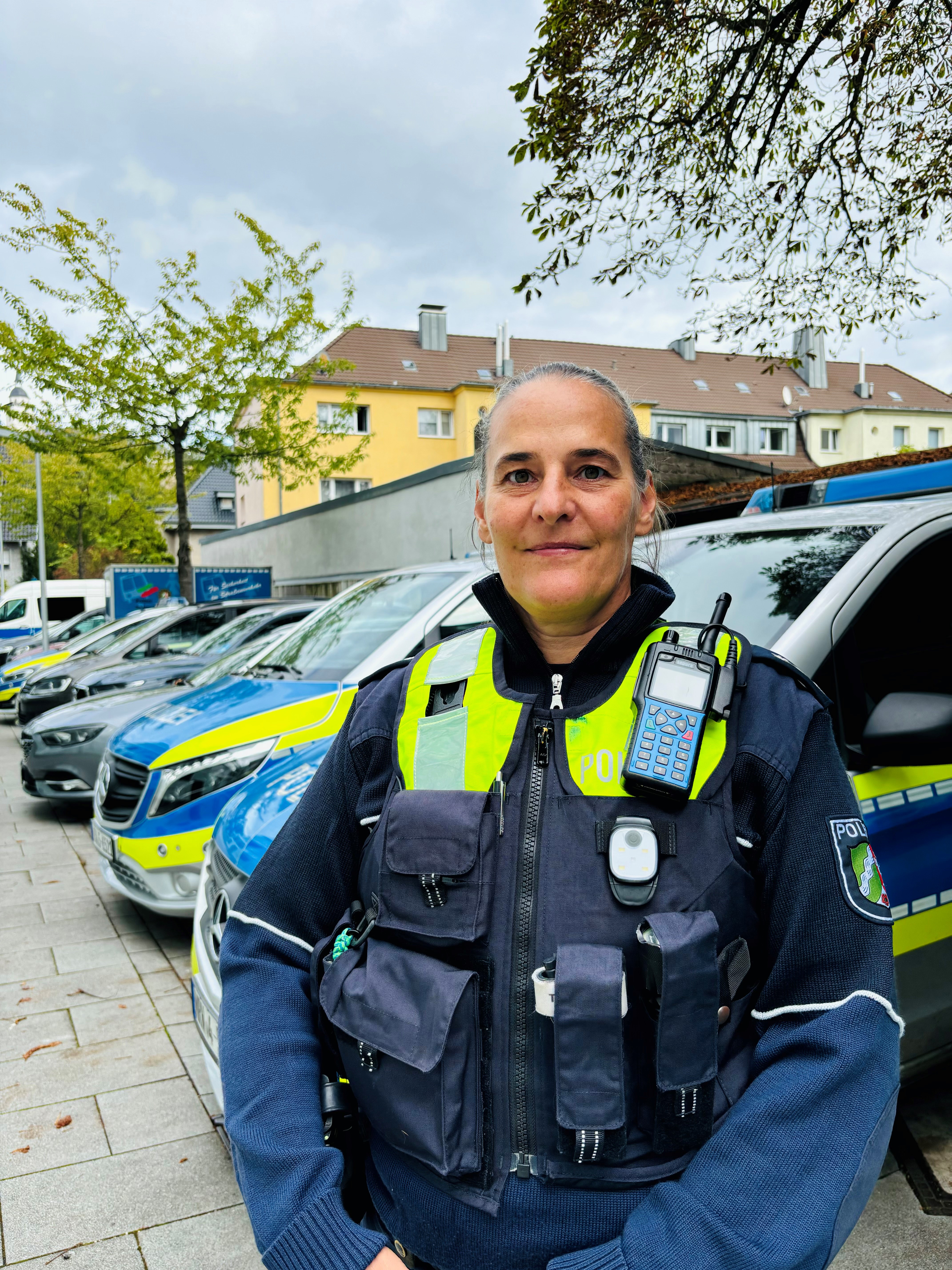 Polizeihauptkommissarin Sandra Schmitz steht vor geparkten Streifenwagen.